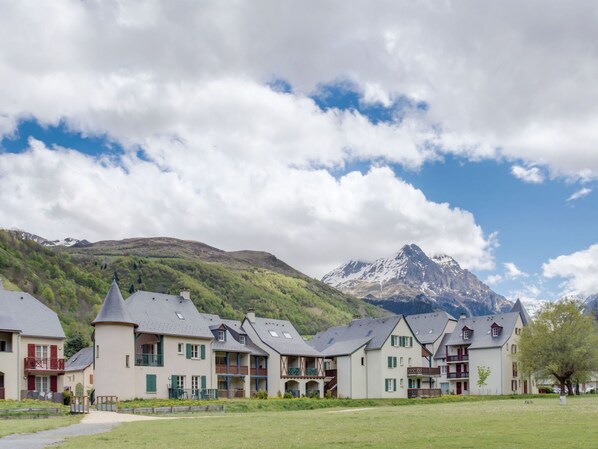 Eine Reihe traditioneller Chalets mit mehreren Stockwerken und Balkonen, vor einer Berglandschaft und einem teils bewölkten Himmel.