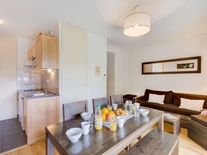 Eine moderne Küche mit Holzschränken, einem Esstisch, der mit Frühstücksleckereien gedeckt ist, und einem dunkelbraunen Sofa im Wohnbereich.