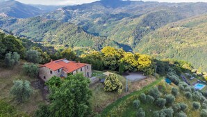 Un edificio de piedra con techo rojo, rodeado de exuberante vegetación y colinas al fondo.