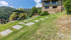 Una casa de piedra con techo inclinado, un patio con mesa y sillas, y un camino de piedra que lleva a la casa.