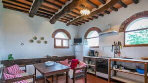A rustic kitchen with exposed wooden beams, a dining area with a wooden table and benches, and a window with a view of greenery. - Podere Piastriccio / Apt.Piccolo by Interhome (Pescia)
