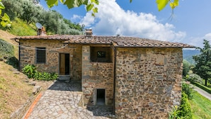 A stone house with a tiled roof, a stone staircase leading to the entrance, and a view of the surrounding landscape. - Podere Zano by Interhome (Pescia)