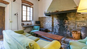 A cozy room with a stone fireplace, a wooden table, and green upholstered chairs. - Podere Zano by Interhome (Pescia)