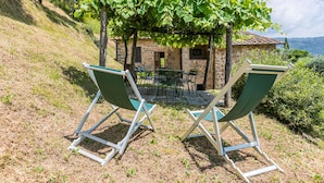 A stone house with a patio, two green lawn chairs, and a view of the countryside. - Podere Zano by Interhome (Pescia)