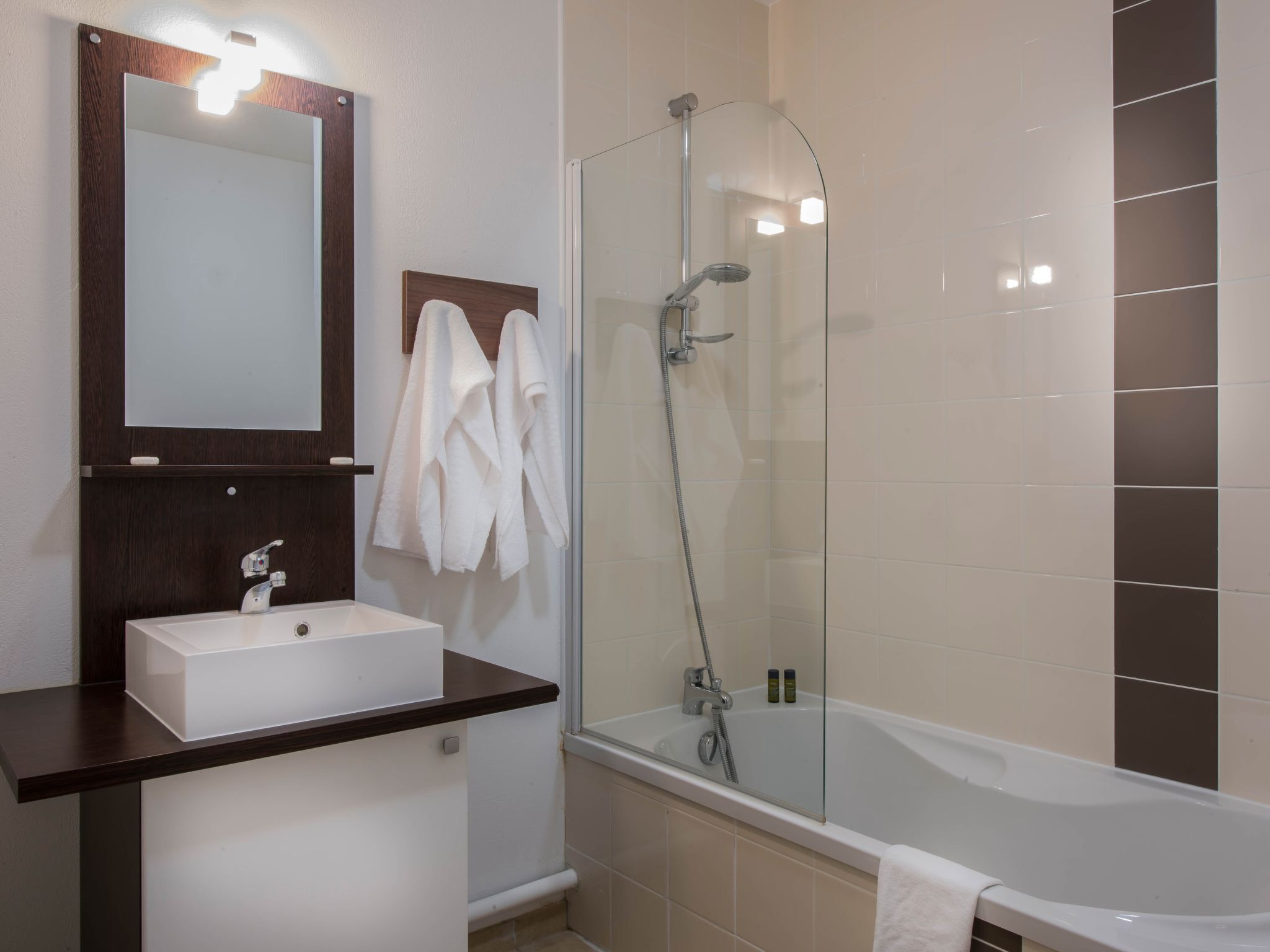 Ein modernes Badezimmer mit einem weißen Waschbecken, einem großen Spiegel und einer gläsernen Duschkabine.