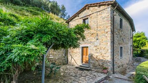 A stone building with a wooden door, a stone staircase, and a garden area with a table and chairs. - Podere Villa / Apt. Gigi by Interhome (Pescia)