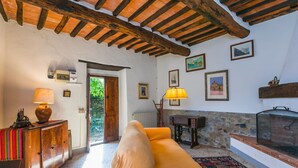 A cozy living room with a sofa, wooden beams, a fireplace, and a stone wall. - Podere Villa / Apt. Gigi by Interhome (Pescia)