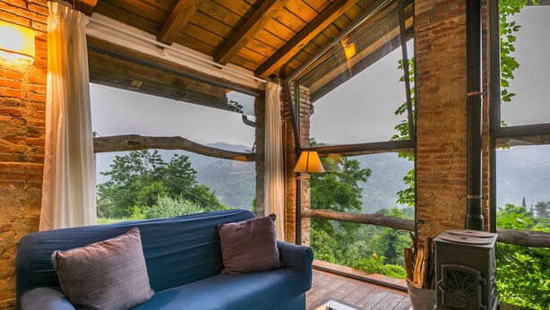 Une pièce chaleureuse avec un canapé bleu, de grandes fenêtres, une cheminée et une vue sur la verdure.