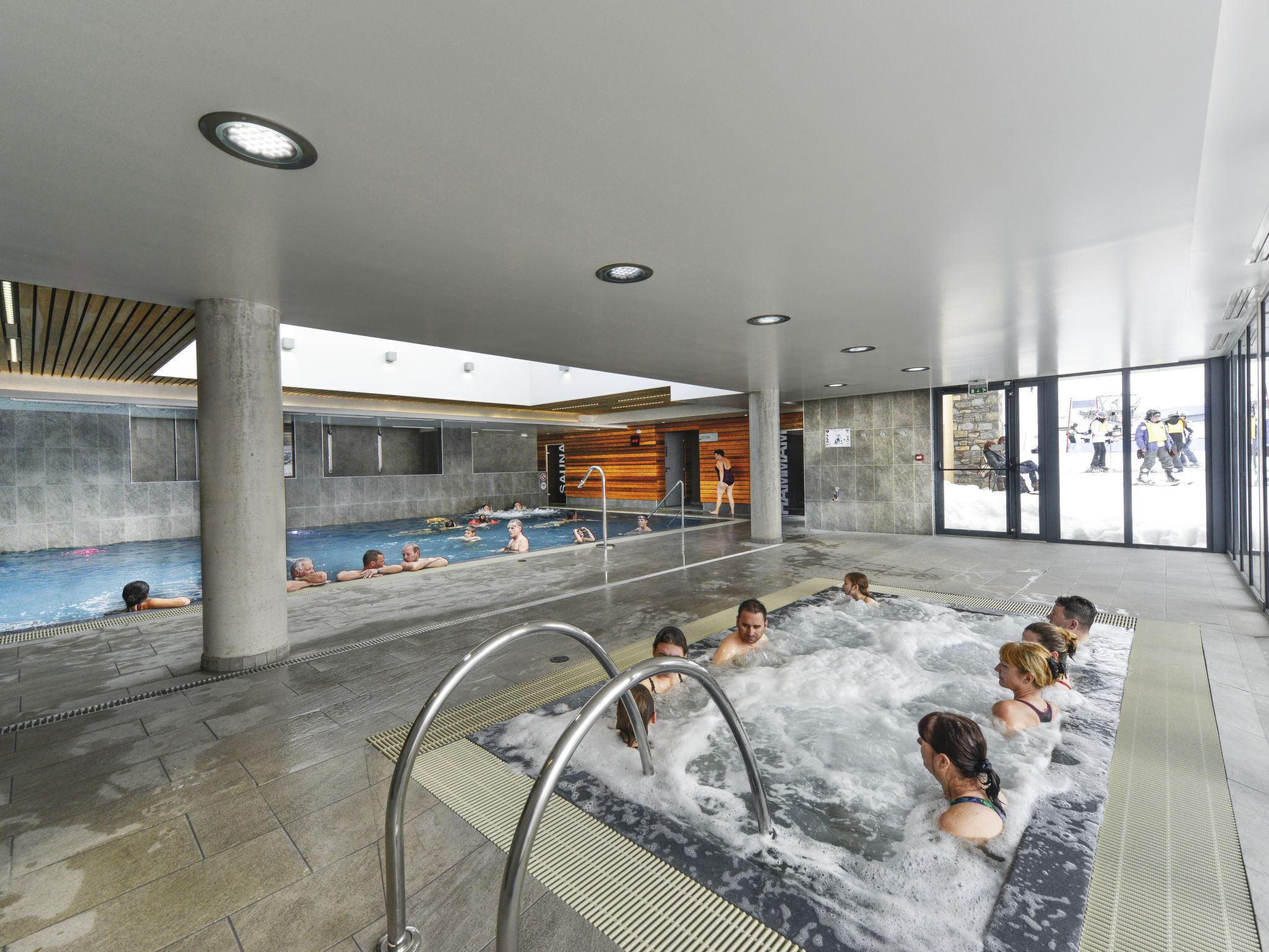 A modern indoor swimming pool with multiple water features, including a hot tub area and a separate pool section.