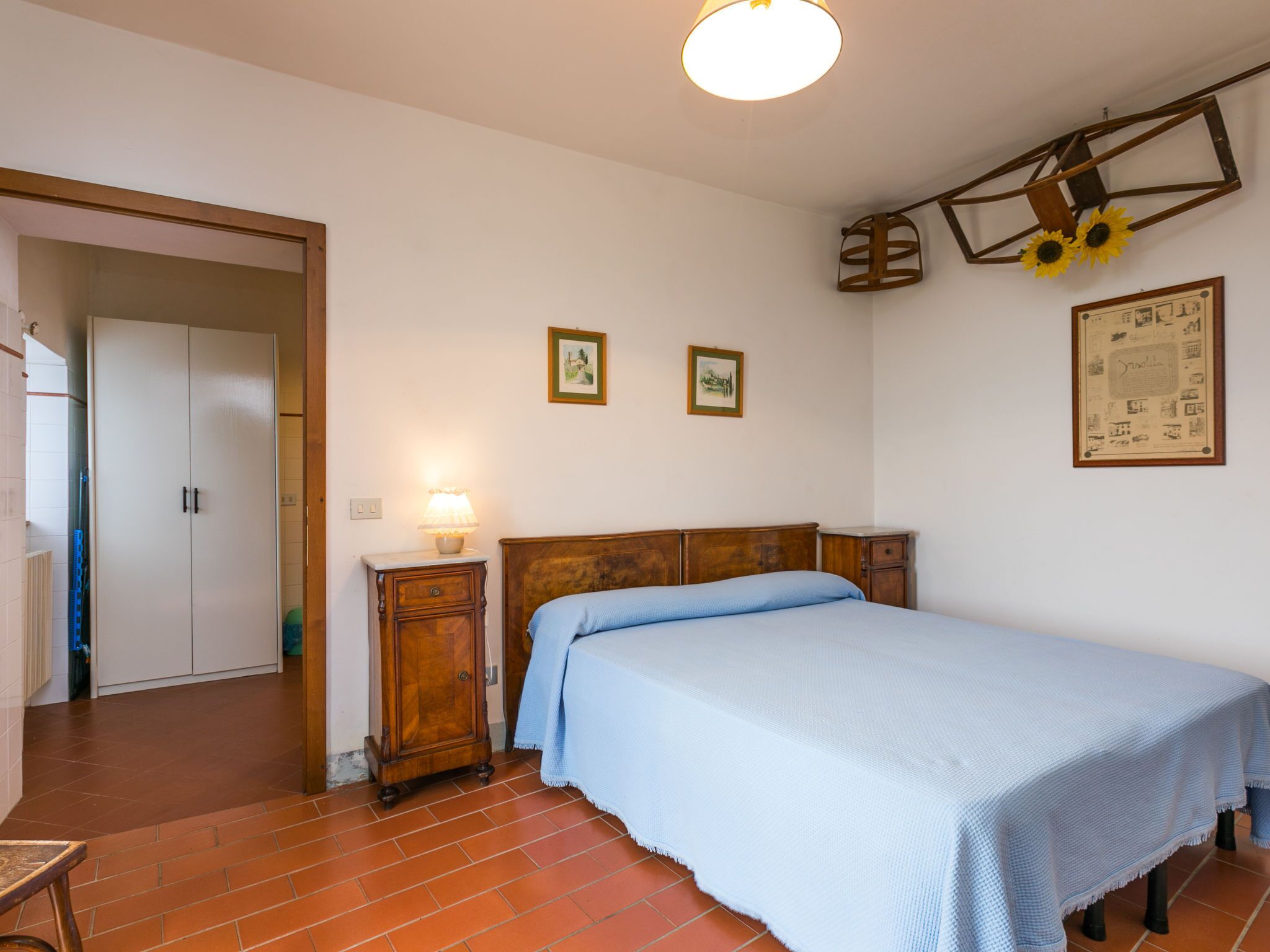 A bedroom with a bed, a nightstand, a wooden wardrobe, and a ceiling light fixture.