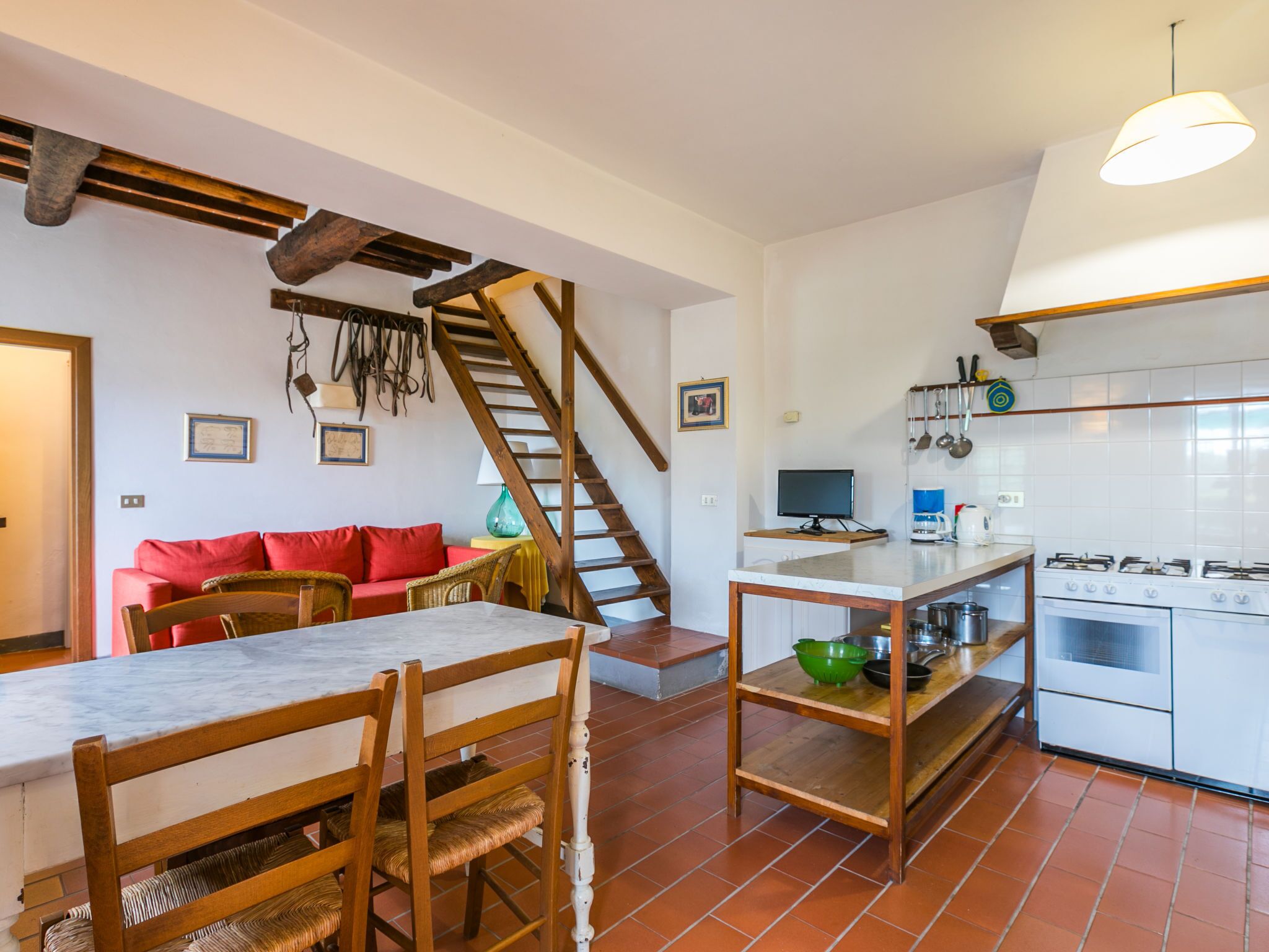 A spacious kitchen with a dining area, a staircase, and a living room with a red sofa.