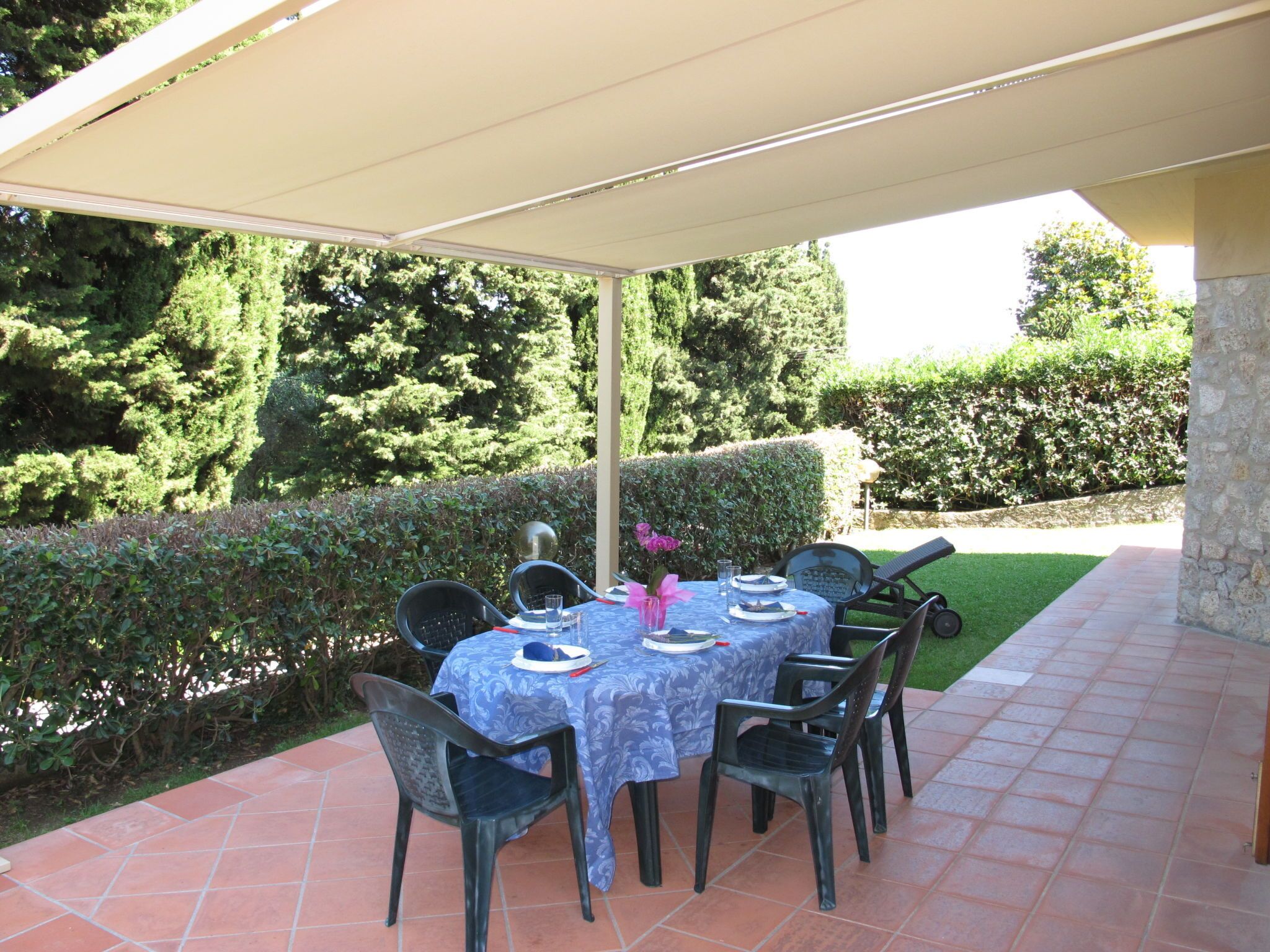 Une terrasse extérieure avec une table dressée pour quatre personnes, entourée de chaises, et protégée par un auvent.