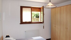 Une chambre à coucher avec un lit, une fenêtre à cadre en bois, un radiateur et une armoire.