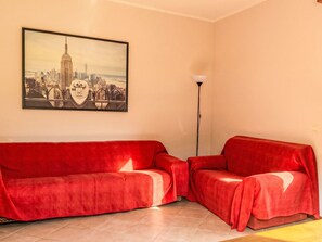 A room with a red sofa, a floor lamp, and a cityscape painting on the wall.