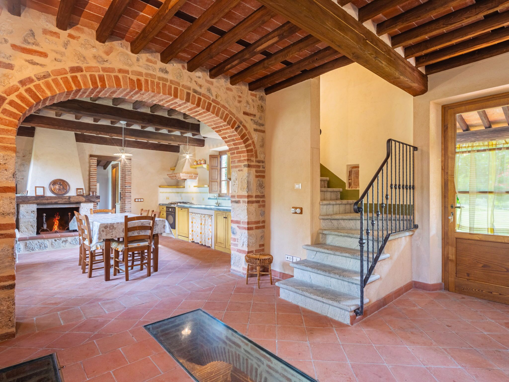 A rustic interior with a stone fireplace, wooden dining table, and a staircase with a metal railing.