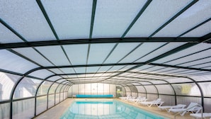 Una piscina interior con paredes de vidrio transparente, agua azul y sillones blancos a los lados.