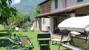 A rustic building with a patio area, outdoor seating, and a mountain in the background. - I Pioppi (CMA107) by Interhome (Camaiore)