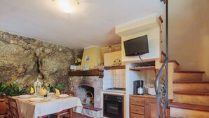 A cozy kitchen with a stone wall, a fireplace, a dining table set for four, and a staircase with a TV above it. - L'Oliveto by Interhome (Camaiore)