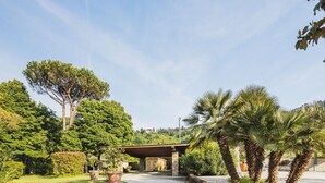 A paved pathway leading to a building with a covered entrance, surrounded by lush greenery and palm trees. - Costacce by Interhome (Camaiore)