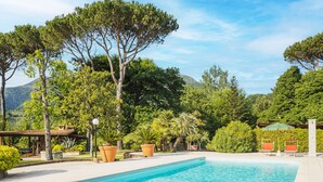 A swimming pool with a curved edge, surrounded by lush greenery and trees. - Costacce by Interhome (Camaiore)