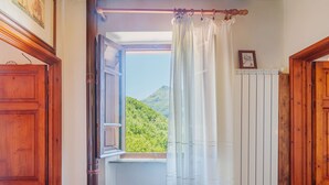A room with a wooden door, a window with a view of green hills, and a radiator. - Paradiso by Interhome (Camaiore)