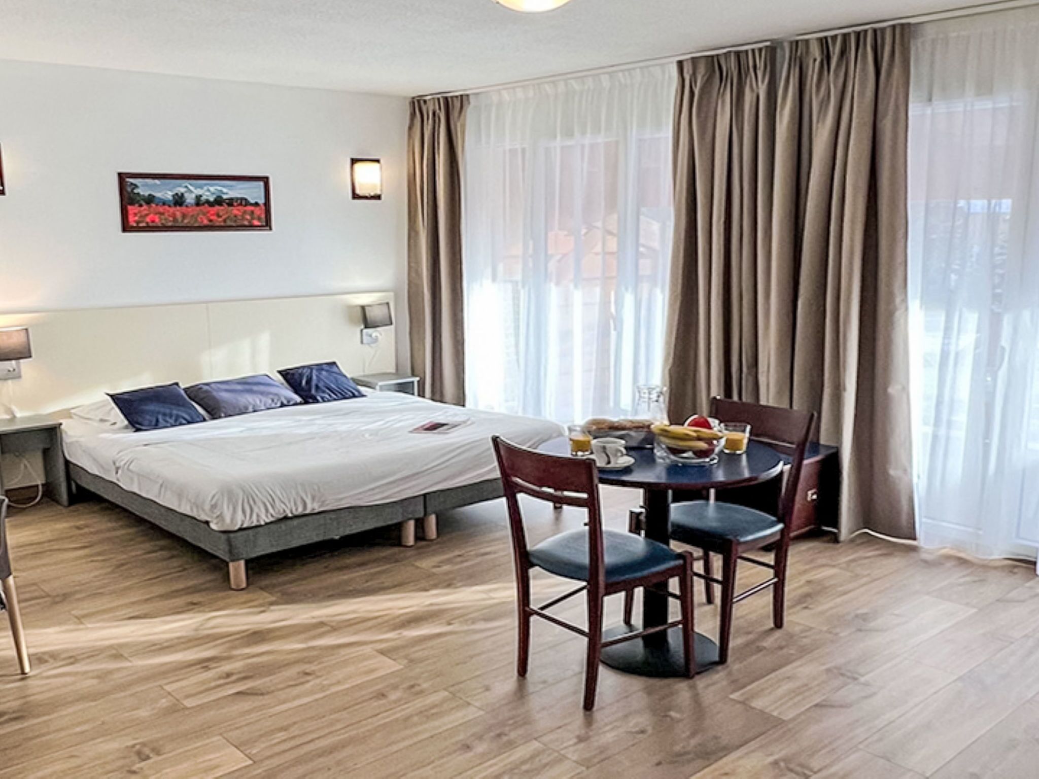 Een hotelkamer met een bed, een eettafel met stoelen, een lamp en een schilderij aan de muur.