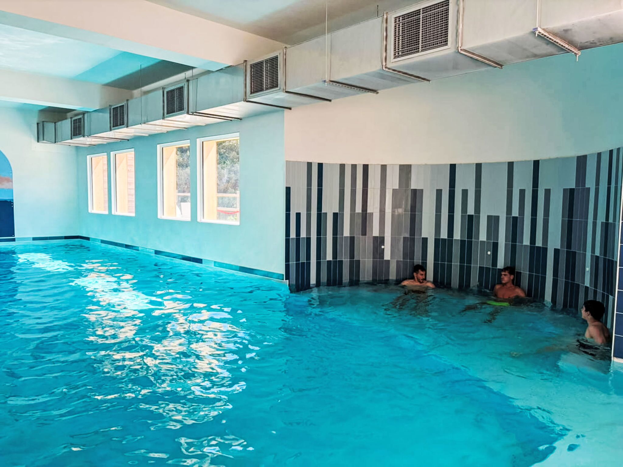 An indoor swimming pool with clear water, tiled walls, and air conditioning units.