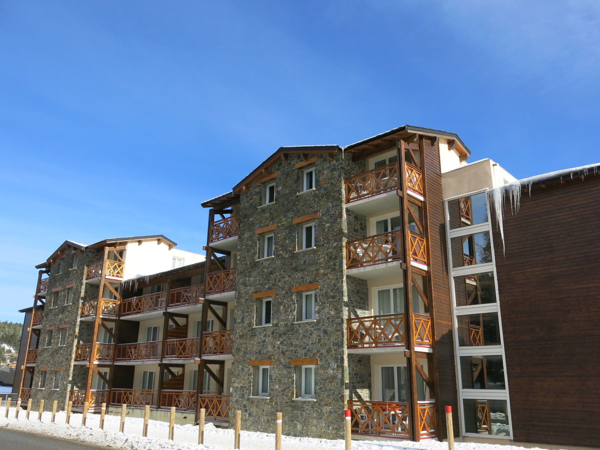 A multi-story hotel with stone and wood exteriors, balconies with wooden railings, and a clear blue sky.