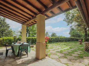 An outdoor patio with stone flooring, a table with chairs, and a pergola overhead.
