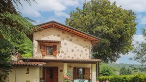 A two-story stone house with a tiled roof, a stone well, and a garden with a table and chairs.