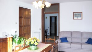 Un comedor con mesa de madera, sillas, un jarrón de flores, un sofá y un cuadro en la pared.