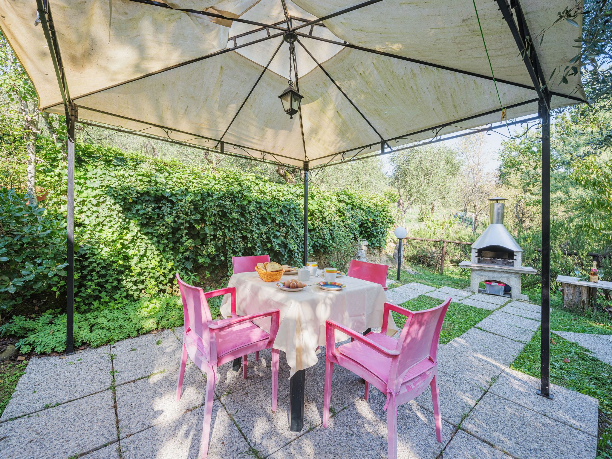 Un patio cubierto con una mesa y sillas, rodeado de vegetación.