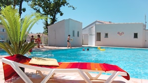 Zona de piscina con sillones de descanso, una mesa con mantel colorido y una bandeja de frutas.