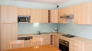 Una cocina compacta con armarios de madera clara, microondas, cafetera, fregadero y estufa.