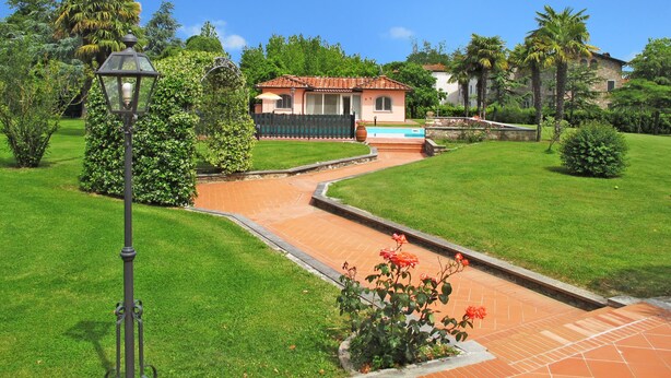 A villa with a tiled pathway leading to a pool, surrounded by lush greenery and palm trees. - Vacation home Teresa by Interhome (Lucca)