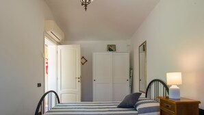 A bedroom with two beds, a wardrobe, a mirror, and a bedside table with a lamp. - Vacation home Teresa by Interhome (Lucca)