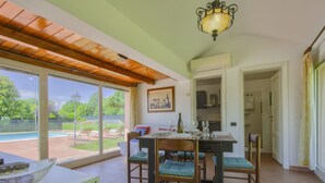 A dining area with a table set for four, chairs, a chandelier, and a view of a swimming pool and garden. - Vacation home Teresa by Interhome (Lucca)