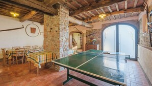 Una habitación rústica con una mesa de ping pong, mesas y sillas de madera, paredes de piedra y un amplio arco de entrada.