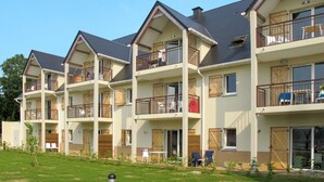 Une rangée d’immeubles résidentiels à plusieurs étages, dotés de balcons, de volets en bois et d’une pelouse verdoyante à l’avant.