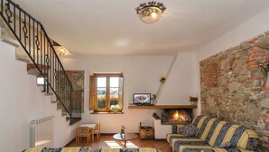 A cozy living room with a fireplace, a sofa set, a dining table with chairs, and a staircase. - Giuseppe by Interhome (Lucca)