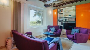 A living room with a fireplace, purple sofas, a coffee table, and a bookshelf. - Rustico dei Canali by Interhome (Lucca)