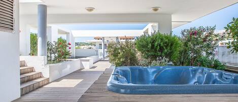 Una terraza en la azotea con jacuzzi, cubierta de madera y plantas en macetas.