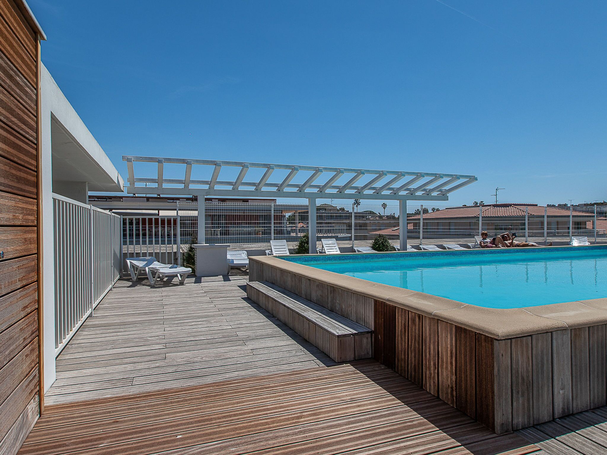 Un espace piscine aménagé sur le toit, avec une terrasse en bois, des chaises longues et une pergola.