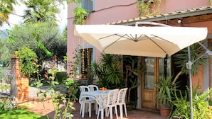 An outdoor patio with a table and chairs under a white umbrella, surrounded by potted plants and a brick wall. - Agrifoglio by Interhome (Lucca)