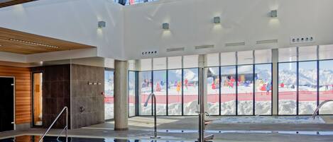 An indoor swimming pool with a view of a snowy outdoor area through large windows.