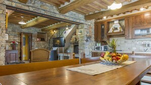 A rustic kitchen with stone walls, wooden beams, and a dining area with a wooden table and chairs.