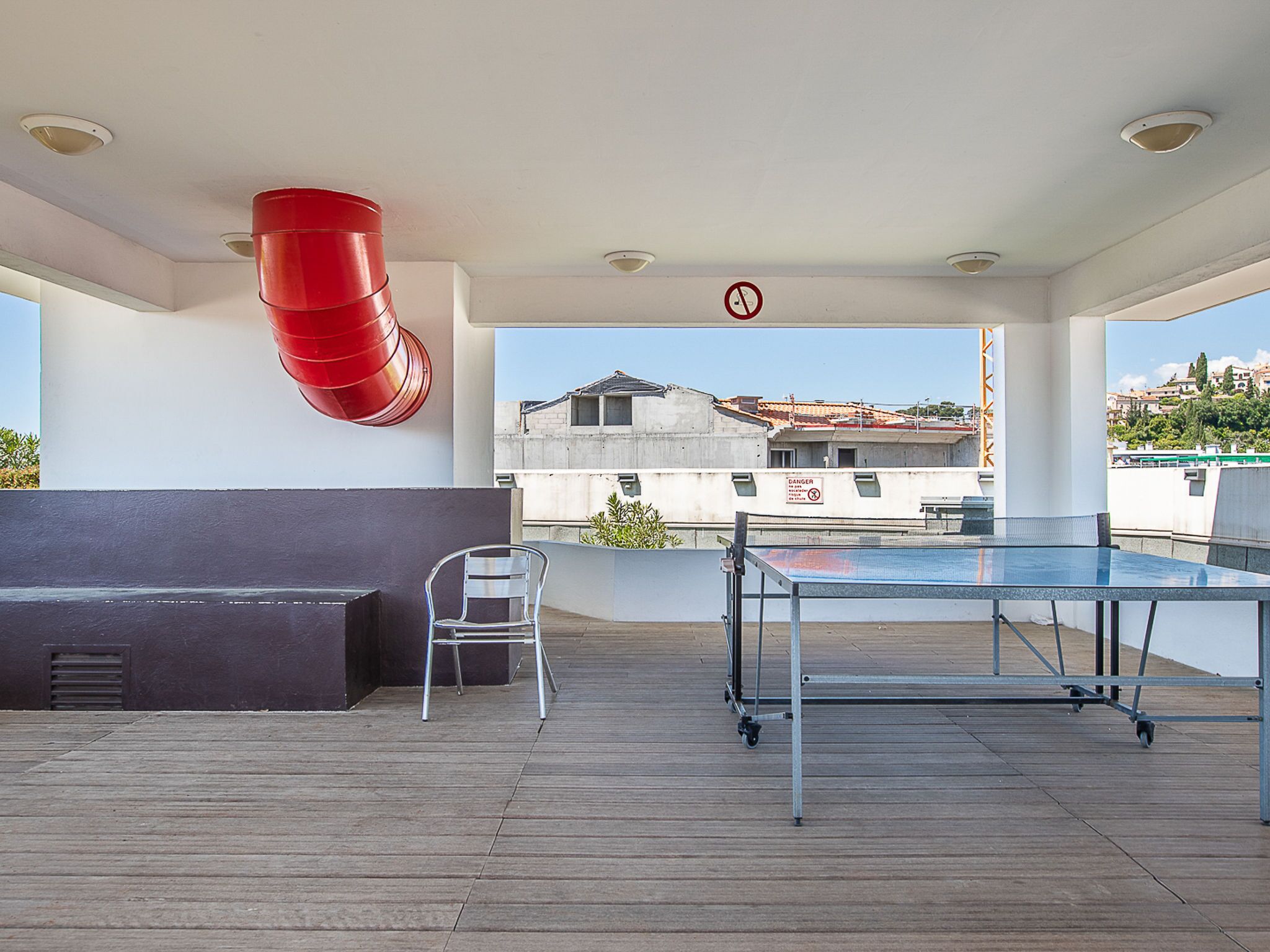 A rooftop terrace with a ping pong table, a metal chair, and a red barrel.