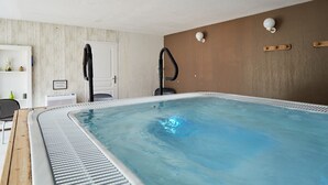 A modern indoor swimming pool with a wooden deck, a black chair, and a white door.