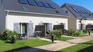 A row of modern houses with solar panels on the roofs, a small patio area with outdoor seating, and a well-maintained lawn.