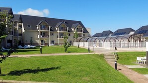 A modern building with multiple balconies, a covered outdoor area, and a grassy courtyard.